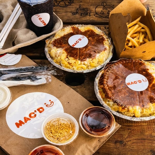 Mac'D mac and cheese pies, fries, drinks, and sauces on a rustic wooden table.