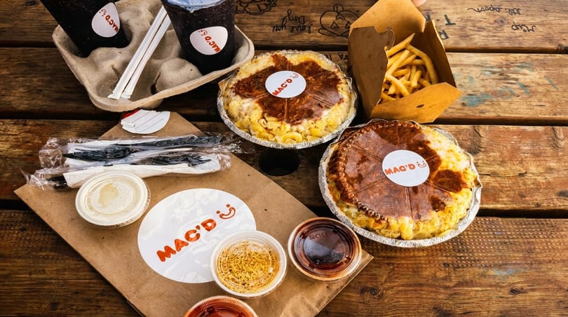 Mac'D mac and cheese pies, fries, drinks, and sauces on a rustic wooden table.