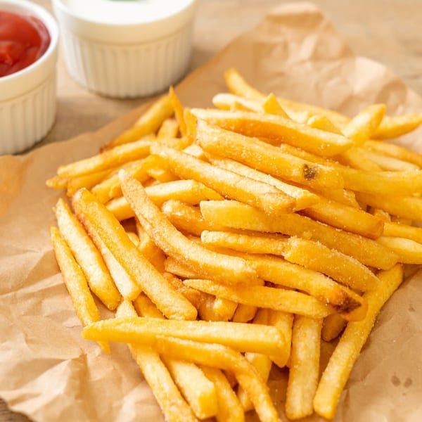 Golden french fries on brown paper with small white bowls of ketchup and mayonnaise.