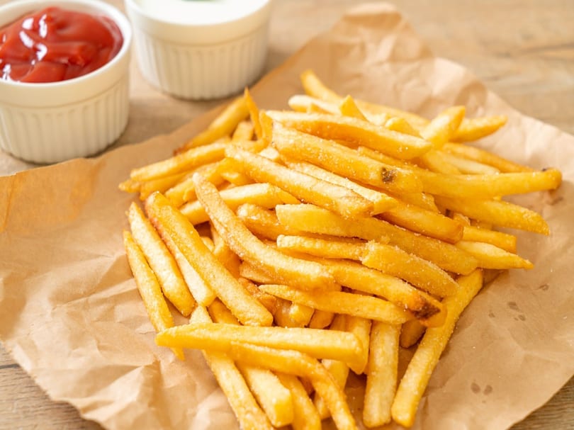 Golden french fries on brown paper with small white bowls of ketchup and mayonnaise.