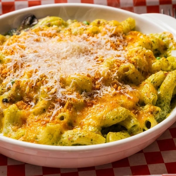 Baked pasta with green sauce, melted cheese, and breadcrumbs in a white dish on a red checkered paper.