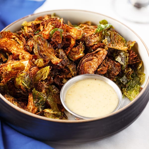 Crispy fried Brussels sprouts with a side of creamy dipping sauce in a black bowl.