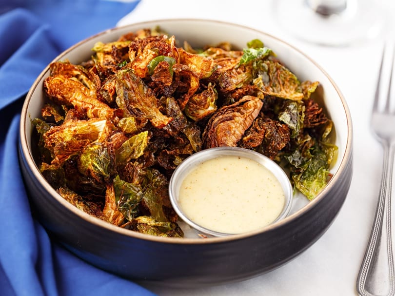 Crispy fried Brussels sprouts with a side of creamy dipping sauce in a black bowl.