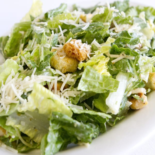 Close-up of a Caesar salad with romaine lettuce, croutons, and shredded Parmesan cheese on a white plate.