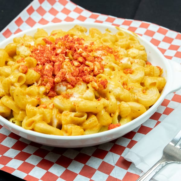 Creamy macaroni and cheese topped with crushed red chips in a white dish on a checkered paper.