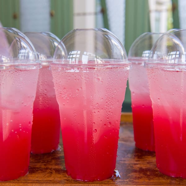 Several plastic cups with dome lids filled with pink and red layered drinks and ice.