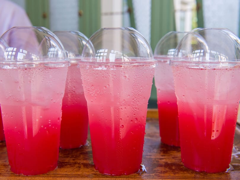 Several plastic cups with dome lids filled with pink and red layered drinks and ice.