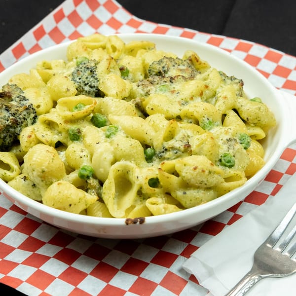 Baked pasta shells with broccoli and peas in a creamy sauce, served in a white dish.