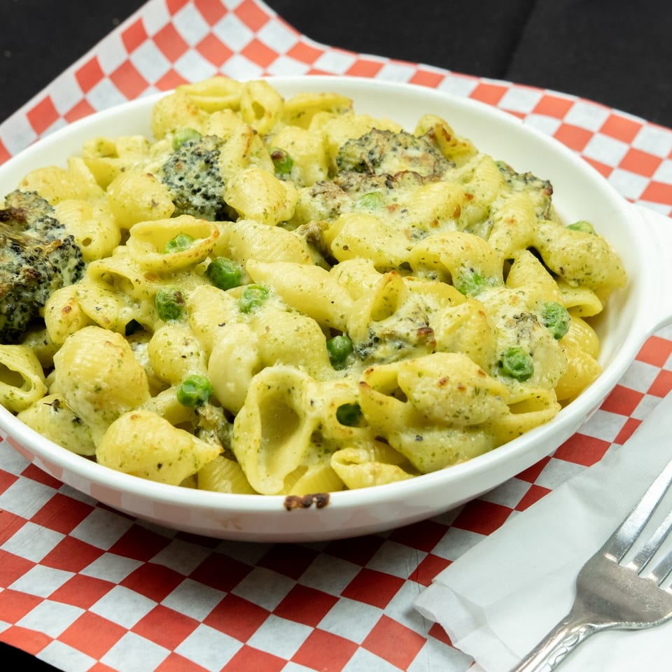 Baked pasta shells with broccoli and peas in a creamy sauce, served in a white dish.