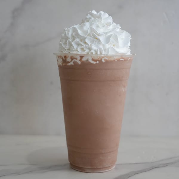 A chocolate milkshake in a clear plastic cup, topped with a generous swirl of white whipped cream.