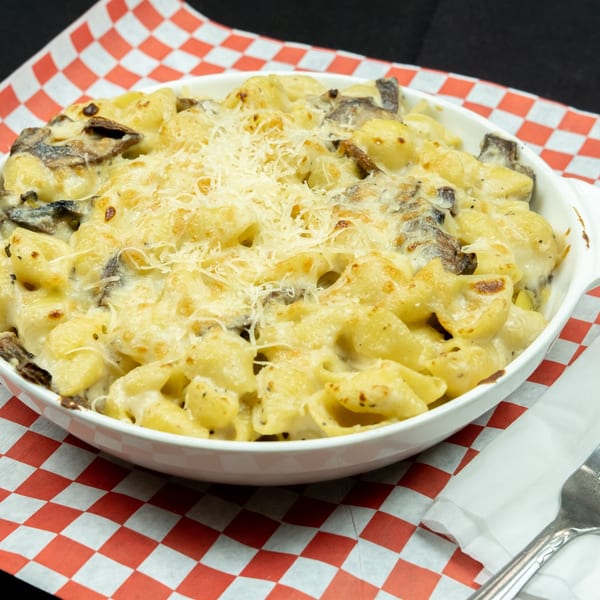 Creamy baked macaroni and cheese with mushrooms, topped with shredded cheese, in a white dish.