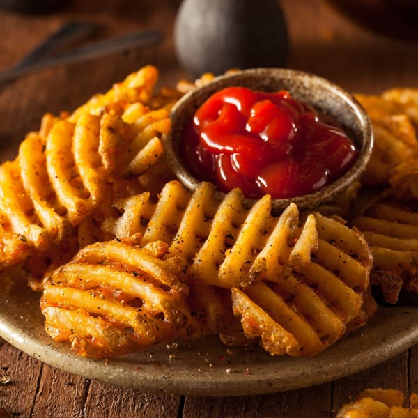 Crispy waffle fries seasoned with pepper, served on a plate with a small bowl of ketchup.