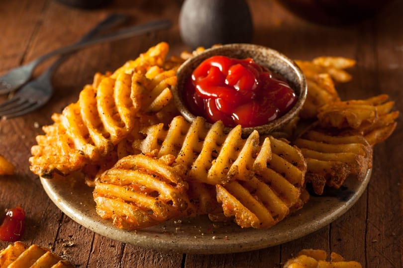 Crispy waffle fries seasoned with pepper, served on a plate with a small bowl of ketchup.
